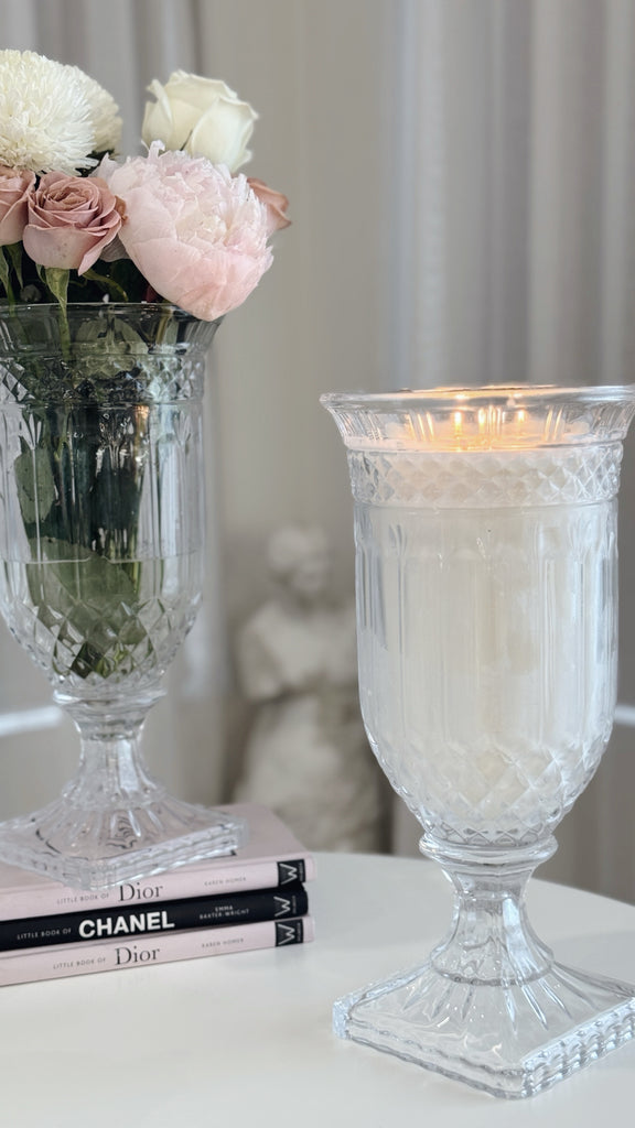 Decorative glass candle holder with a lit candle next to a vase of flowers on books.